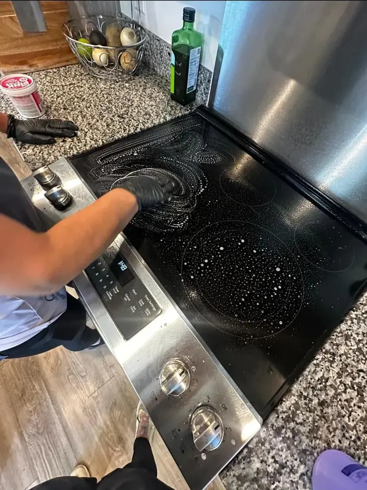 Clean Lean Services team member scrubbing a glass stovetop during a kitchen cleaning